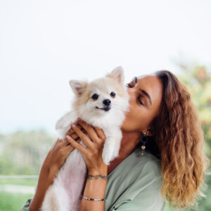 outdoor portrait curly european tanned woman holds happy pet dog pomeranian spitz
